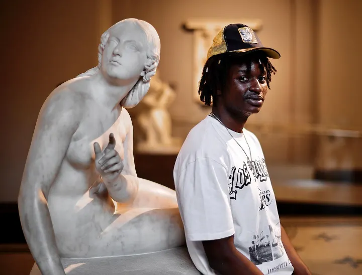 Male model in a gallery posed beside a classical marble sculpture