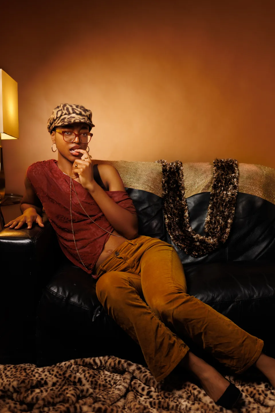 Warm editorial portrait of a model in rich autumnal styling seated on a dark leather sofa
