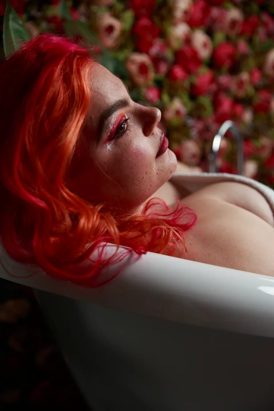 Red-haired woman reclining in a floral bath setting